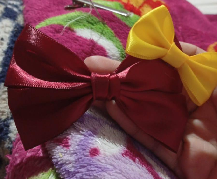 imagem de um laço de cabelo vermelho com um laço amarelo menor na ponta e pedrinhas decorativas