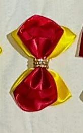 imagem de um laço de cabelo amarelo com um laço vermelho sobreposto e pedrinhas decorativas no nó do laço